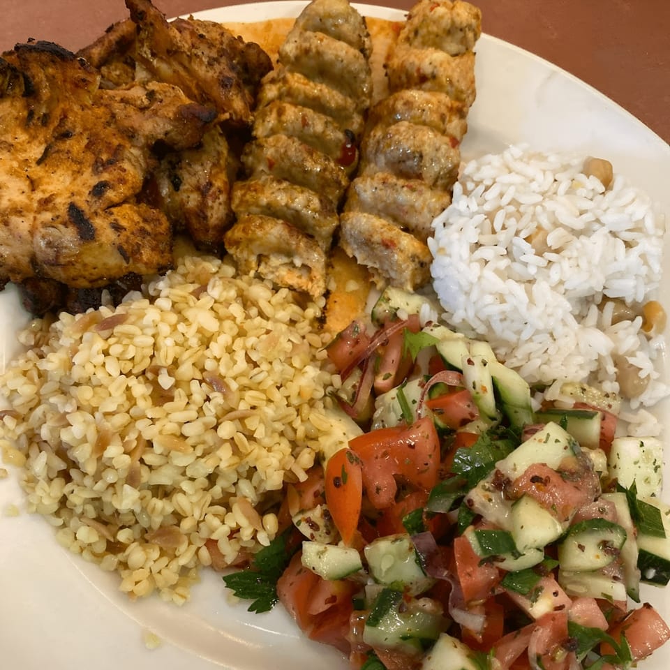 A Turkish platter with grilled chicken, kebab skewers, rice, bulgur, and a fresh salad.