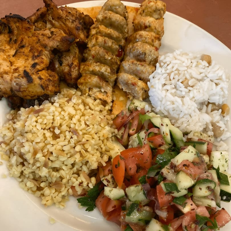 A Turkish platter with grilled chicken, kebab skewers, rice, bulgur, and a fresh salad.