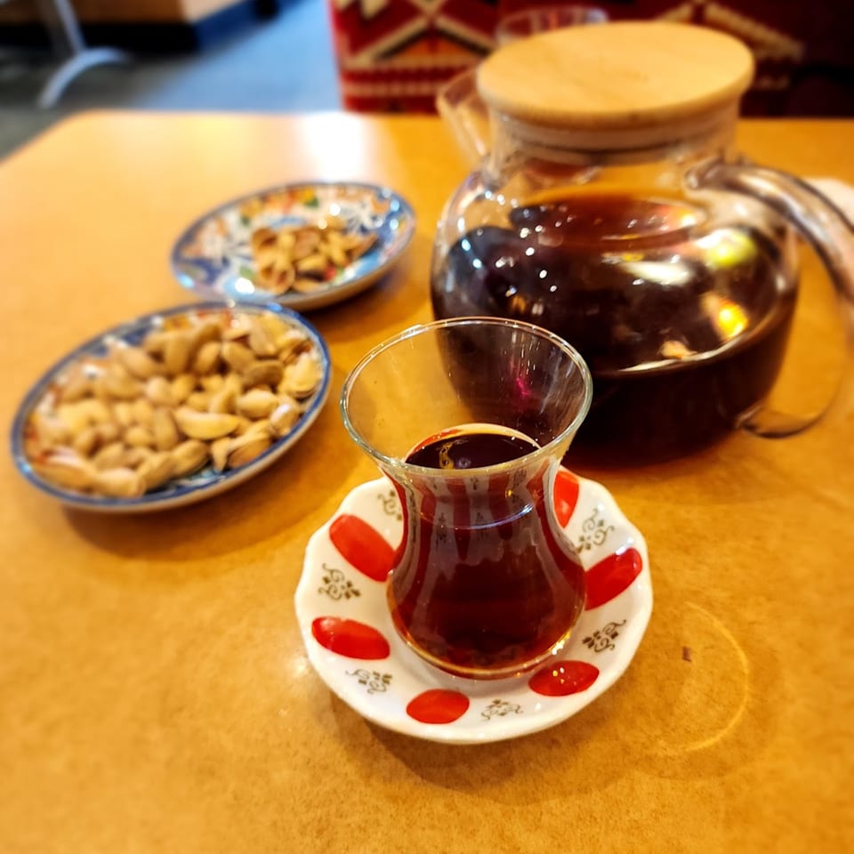 Turkish tea in a traditional glass and teapot, with two small plates of nuts on a wooden table.