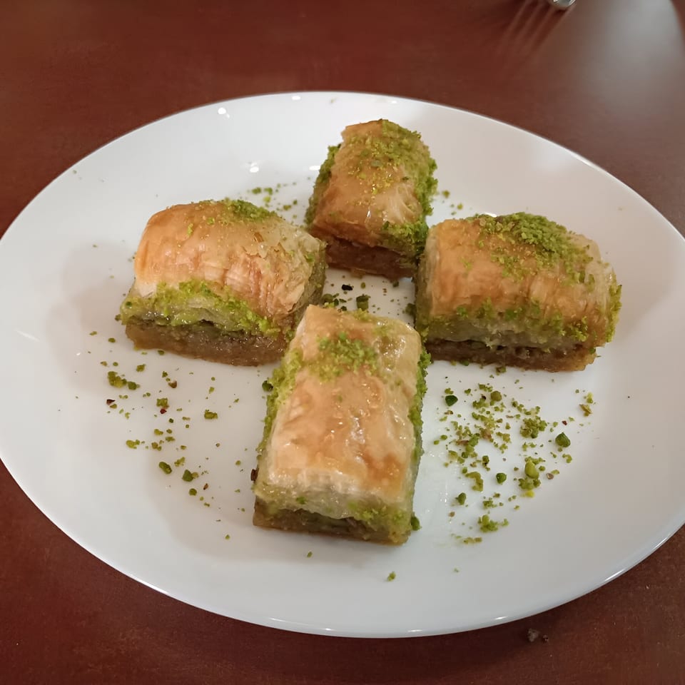 Four pieces of Turkish baklava, topped with crushed pistachios, on a white plate.