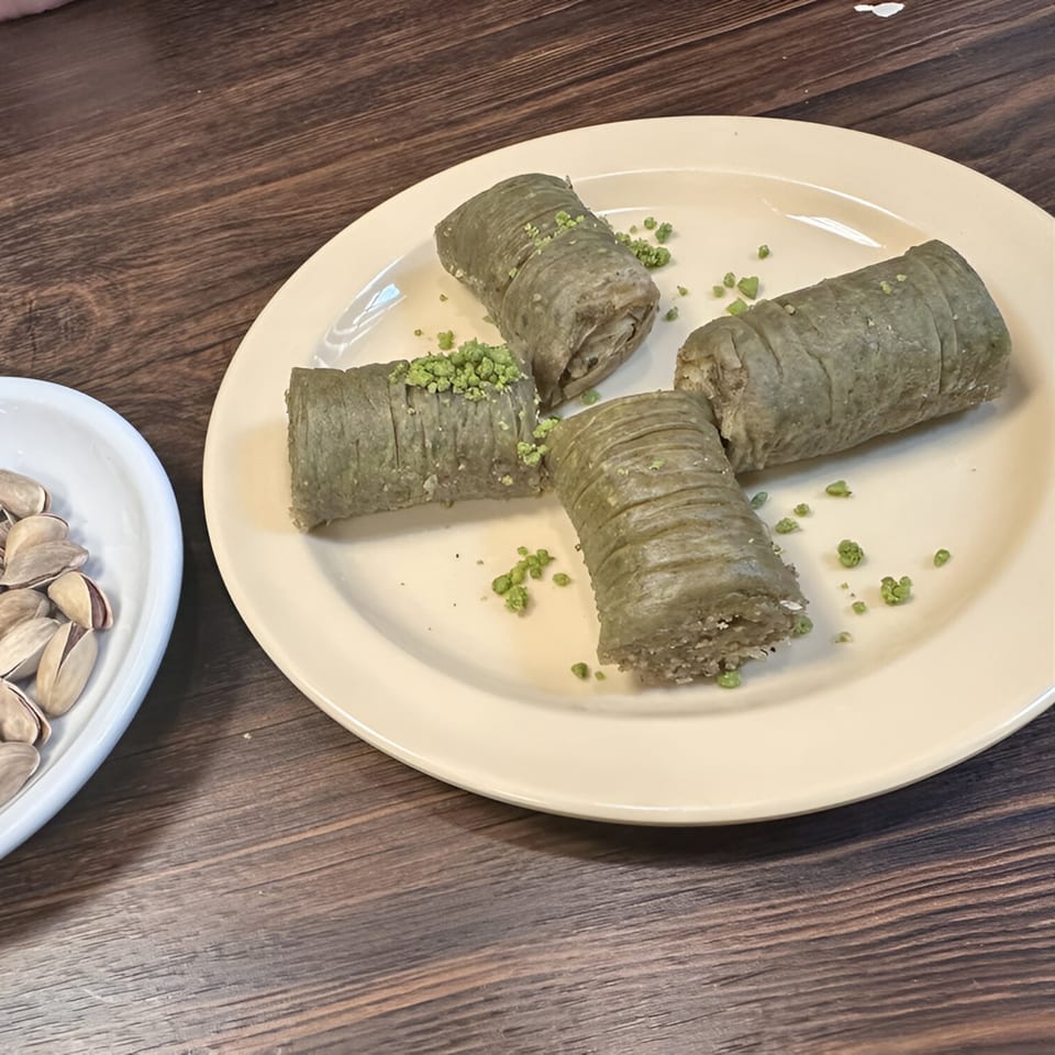 Four pieces of green pistachio baklava on a plate, with a side of pistachios in shells.