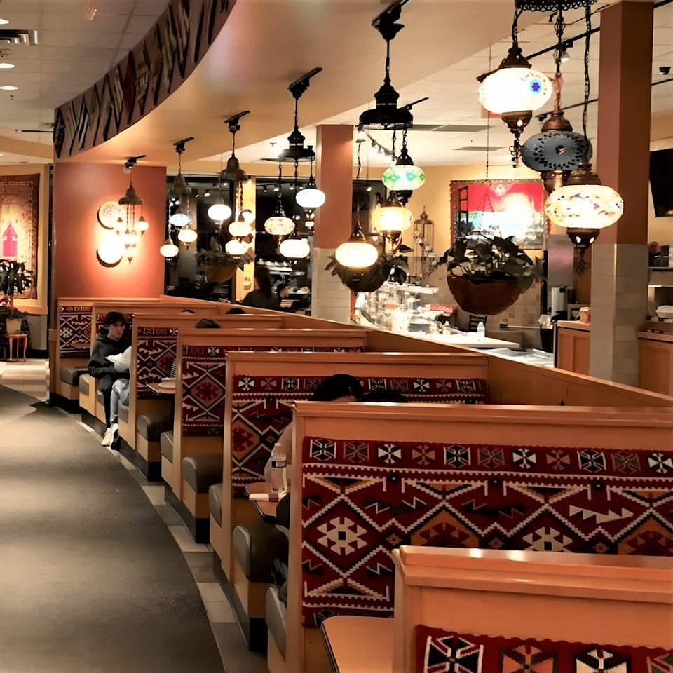 Turkish restaurant interior with ornate hanging lamps, patterned booth seating, and a few patrons.