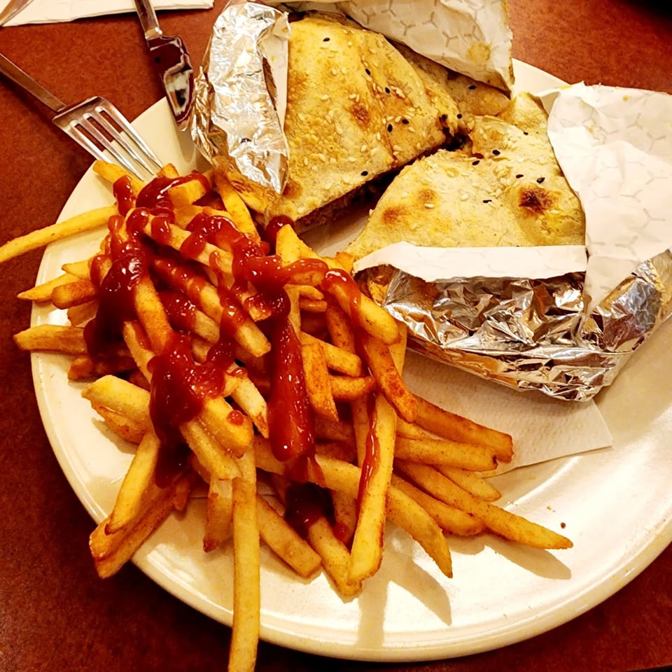 Turkish flatbread wraps with sesame seeds, partially wrapped in foil, served with ketchup-covered fries.