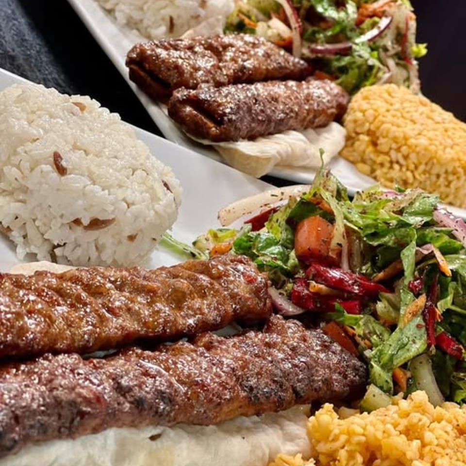 Two plates of Turkish kebabs with rice, salad, and bulgur, served on white rectangular dishes.